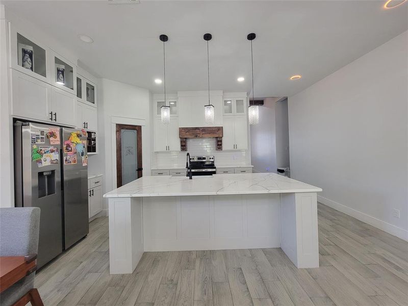 Kitchen featuring glass insert cabinets, stainless steel appliances, white cabinets, a spacious island, and hanging light fixtures