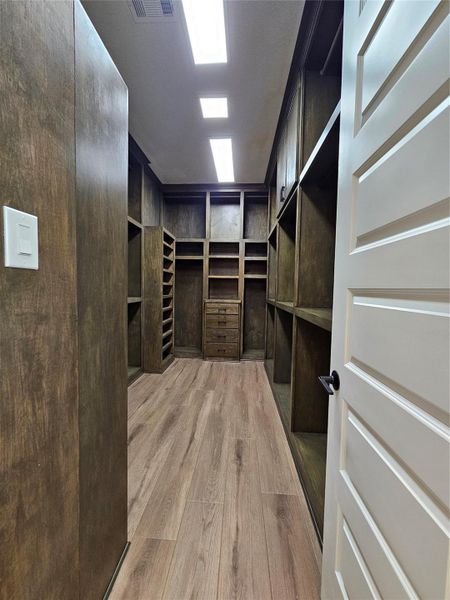 Spacious walk-in closet with wooden shelving and drawers, ample storage, and bright overhead lighting.