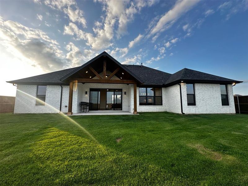 Rear view of property featuring a lawn, brick siding, a patio, and a shingled roof