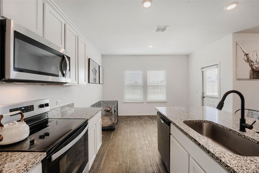 Modern kitchen featuring a large island with an undermount sink and black faucet, granite countertops, stainless steel appliances, white cabinetry, and wood-finish flooring Modern kitchen featuring a large island with an undermount sink and black faucet, granite countertops, stainless steel appliances, white cabinetry, and wood-finish flooring