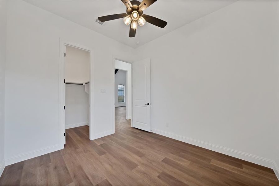Secondary bedroom with a walk in closet, wood finished floors, and a ceiling fan