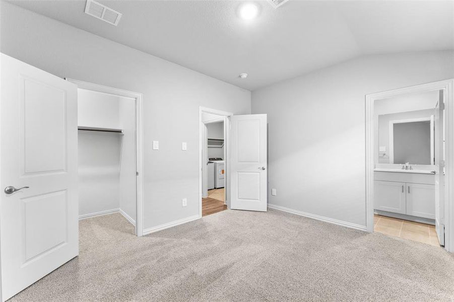 Unfurnished bedroom with a walk in closet, light carpet, lofted ceiling, washer and dryer, and ensuite bath Unfurnished bedroom with a walk in closet, light carpet, lofted ceiling, washer and dryer, and ensuite bath