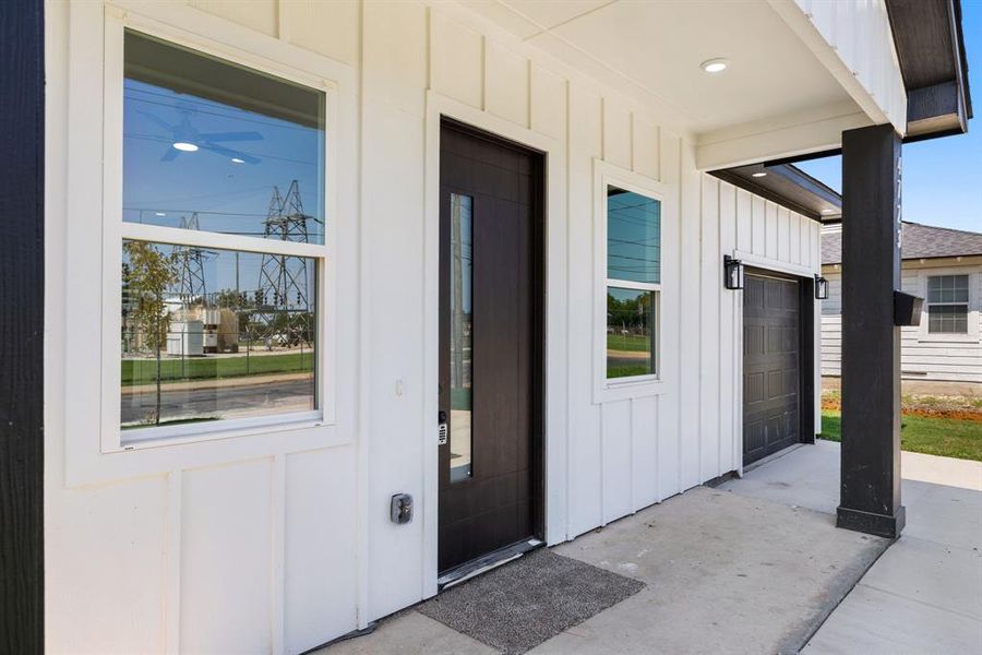 Property entrance with board and batten siding, a garage, covered porch, and concrete driveway