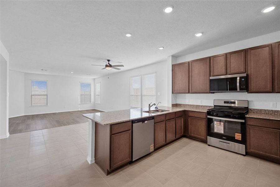 The kitchen features high ceilings, stained wood cabinets, granite countertops, SS appliances including microwave, modern tile backsplash, recessed lighting, and a pantry all overlooking your huge Great Room.