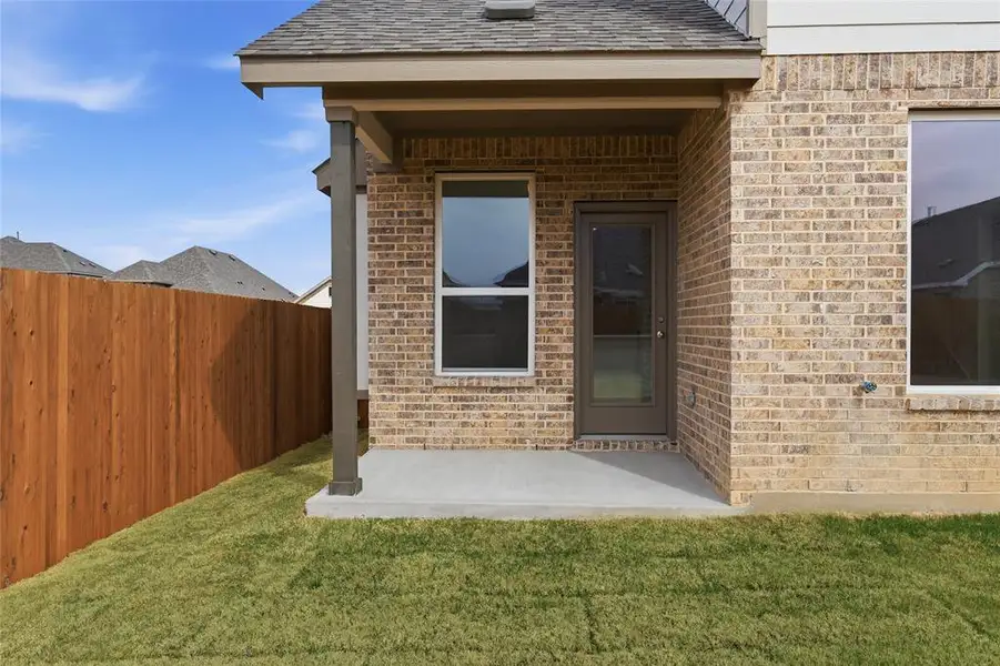 Entrance to property featuring a patio, brick siding, and roof with shingles
