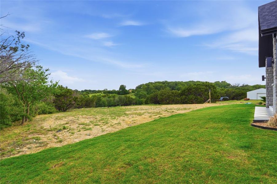 Expansive green lawn bordering a natural landscape with mature trees and a distant building