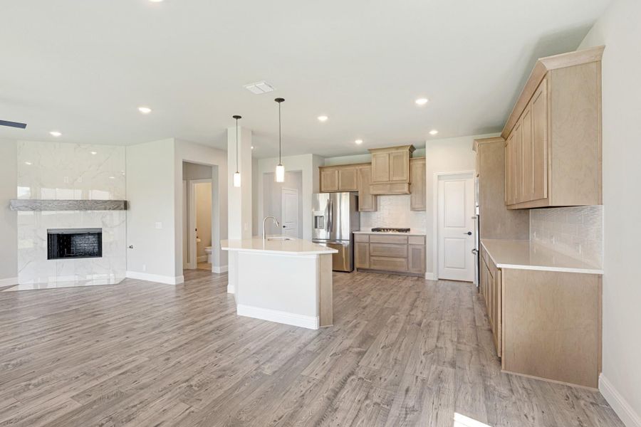 Open-concept kitchen with light wood cabinets, center island, and hardwood floors, open to living area with fireplace.