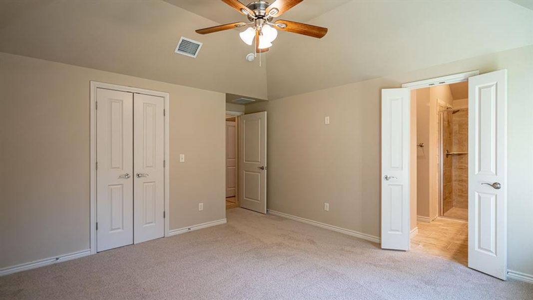 Unfurnished bedroom with light colored carpet, a closet, ensuite bath, ceiling fan, and vaulted ceiling