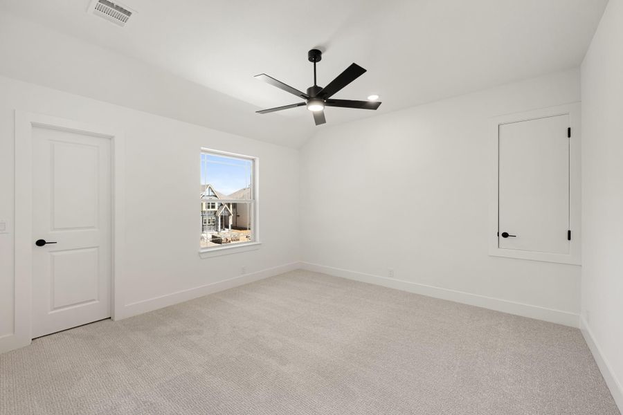 Empty bedroom with vaulted ceiling, black ceiling fan, carpet flooring, and white walls
