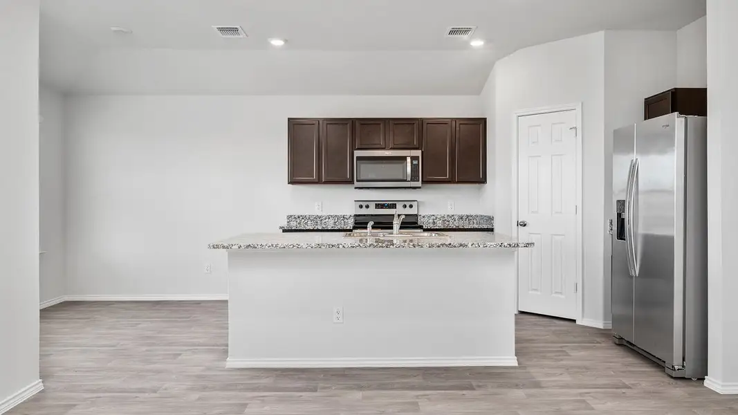 Kitchen featuring stainless steel appliances, dark wood finish cabinets, light stone counters, light wood-style flooring, and vaulted ceiling
