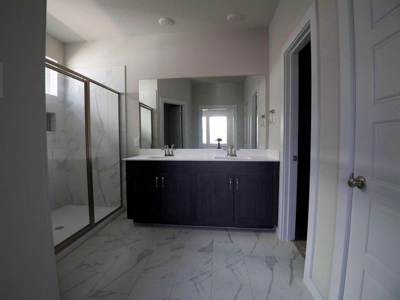 Full bath featuring plenty of natural light, light marble finish flooring, a marble finish shower, and double vanity Full bath featuring plenty of natural light, light marble finish flooring, a marble finish shower, and double vanity