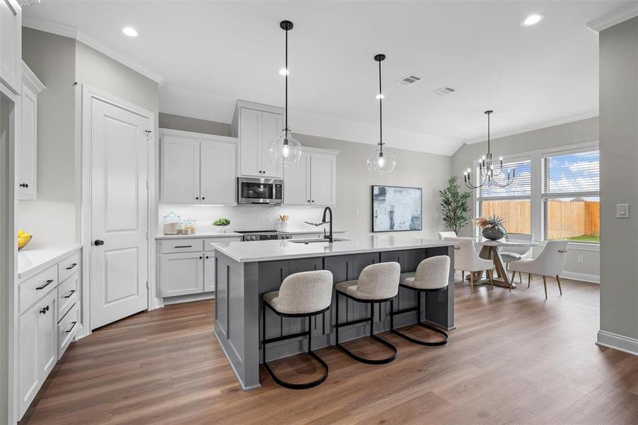 Kitchen with a breakfast bar, white cabinets, decorative light fixtures, an island with sink, and tasteful backsplash Kitchen with a breakfast bar, white cabinets, decorative light fixtures, an island with sink, and tasteful backsplash