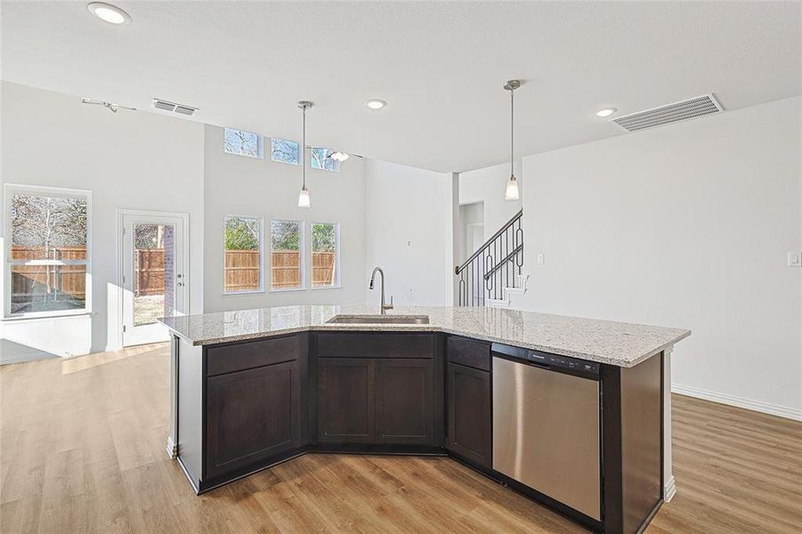 Kitchen featuring dark brown cabinets, sink, a center island with sink, dishwasher, and hanging light fixtures