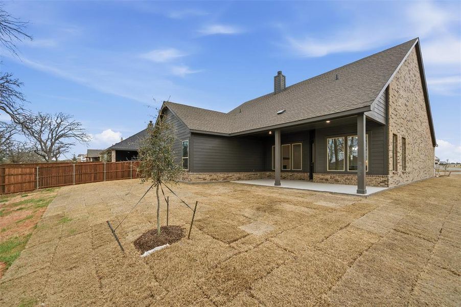 Rear view of property with a patio, a shingled roof, a chimney, a fenced backyard, and stone siding Rear view of property with a patio, a shingled roof, a chimney, a fenced backyard, and stone siding