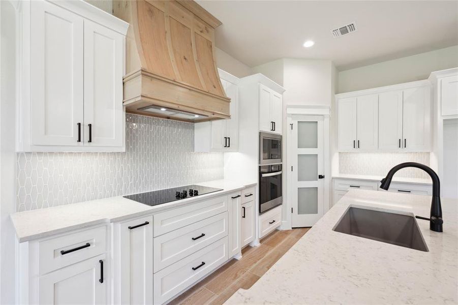 Kitchen with custom exhaust hood, black electric cooktop, sink, light hardwood / wood-style flooring, and white cabinets