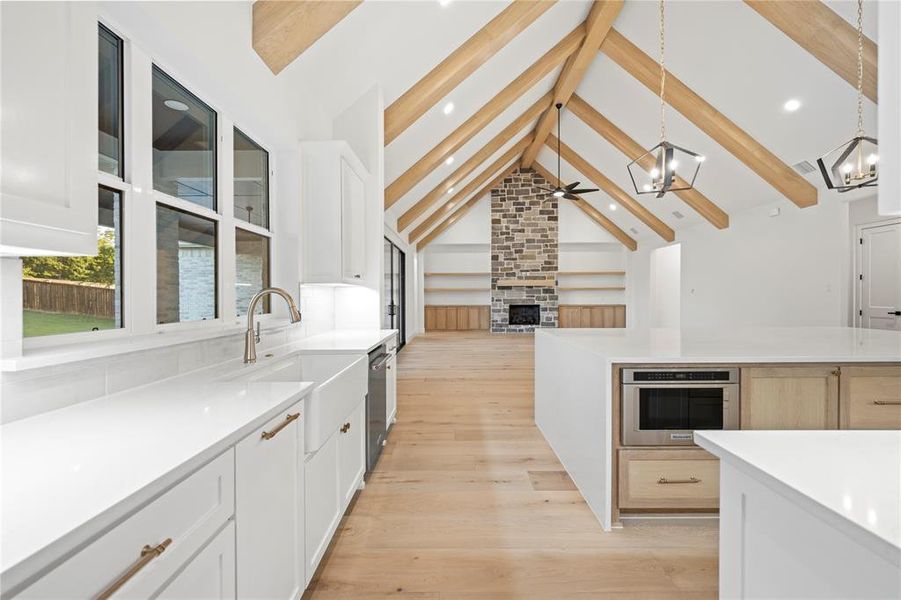 Kitchen with a large fireplace, light stone counters, open floor plan, beam ceiling, and light wood-style floors Kitchen with a large fireplace, light stone counters, open floor plan, beam ceiling, and light wood-style floors