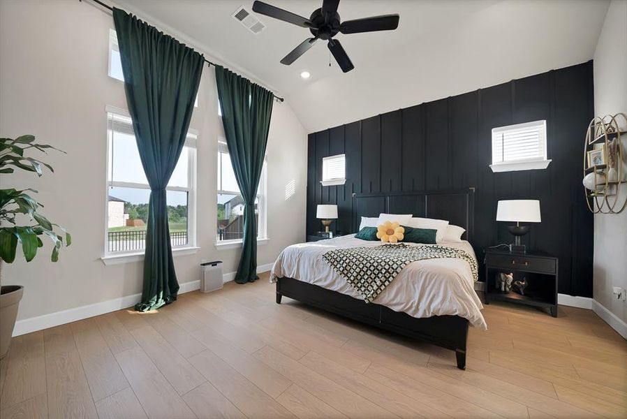 Spacious bedroom featuring vaulted ceilings, light wood-finish flooring, and a striking accent wall with vertical paneling Spacious bedroom featuring vaulted ceilings, light wood-finish flooring, and a striking accent wall with vertical paneling