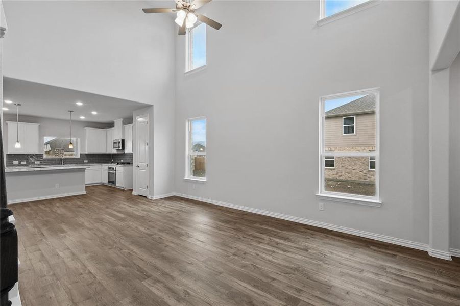 Unfurnished living room featuring a ceiling fan, a towering ceiling, and dark wood-style flooring