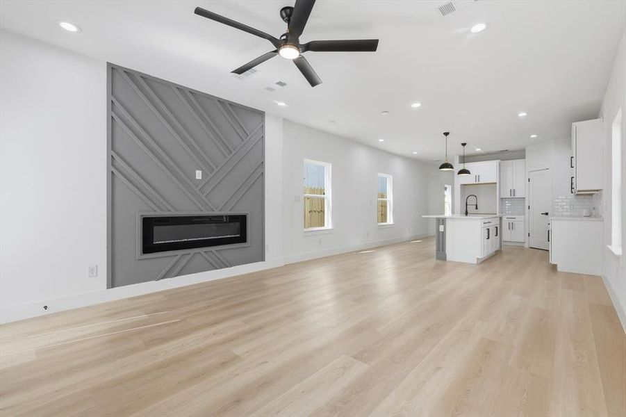 Unfurnished living room featuring a ceiling fan, light wood finished floors, recessed lighting, and a large fireplace
