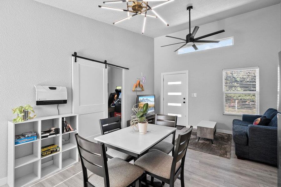Dining area featuring a barn door, a high ceiling, light wood-style flooring, and a ceiling fan.