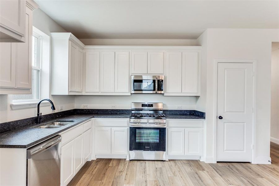 Kitchen featuring stainless steel appliances, sink, white cabinetry, and light wood-type flooring