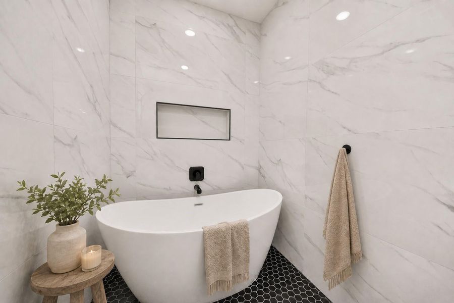 Elegant freestanding soaking tub surrounded by floor-to-ceiling marble-look tile, creating a serene spa-inspired retreat.