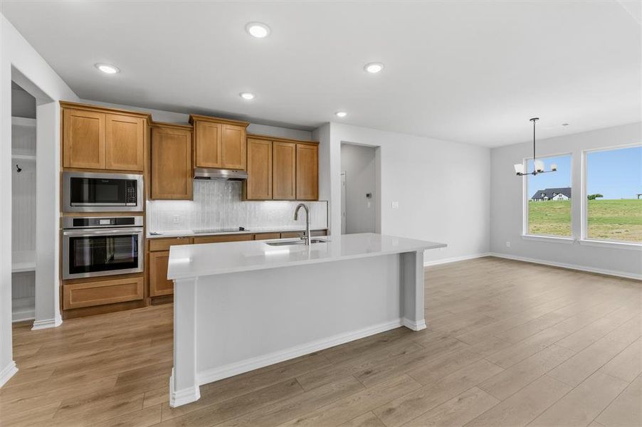 Kitchen featuring wood finish cabinetry, stainless steel appliances, light wood-style flooring, and a center island with sink