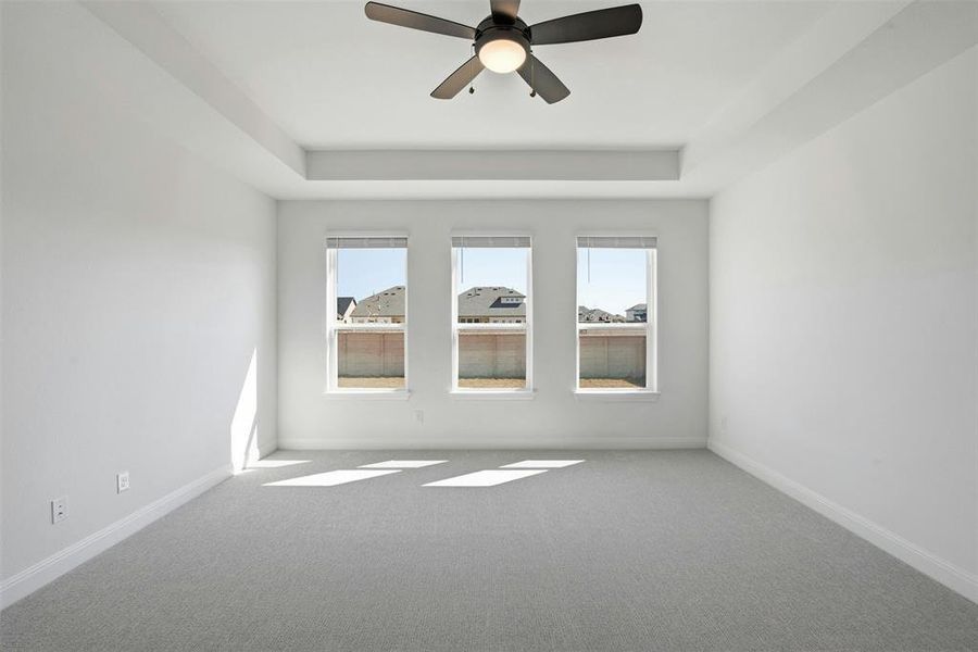 Bright room featuring a tray ceiling with a ceiling fan, light gray carpeting, and three transom windows
