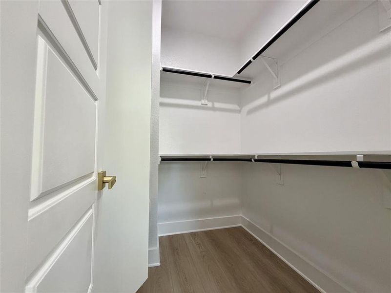 Primary Walk-in closet featuring wood-finish flooring, white walls, and built-in shelving with hanging rods Primary Walk-in closet featuring wood-finish flooring, white walls, and built-in shelving with hanging rods