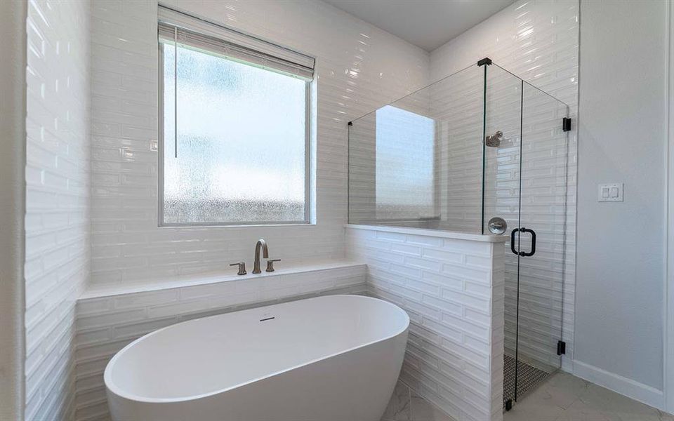 Freestanding soaking tub with brushed nickel fixtures, complemented by a large walk-in shower with clear glass enclosure and linear tile floor Freestanding soaking tub with brushed nickel fixtures, complemented by a large walk-in shower with clear glass enclosure and linear tile floor