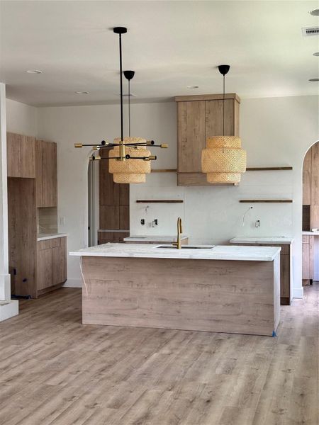 Spacious modern kitchen with wood cabinetry, a large island, and pendant lighting. Features sleek countertops and open shelving, creating a warm, inviting atmosphere.