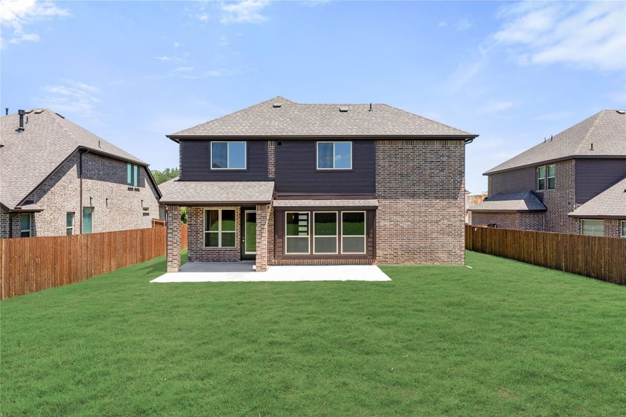 Two-story brick home rear view with covered patio, large green lawn, and wood privacy fence