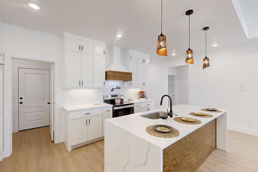 Kitchen with stainless steel electric range oven, sink, white cabinetry, custom range hood, and an island with sink