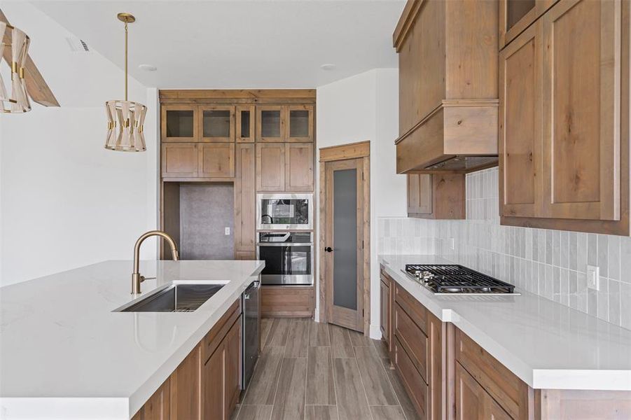 Kitchen with sink, hanging light fixtures, stainless steel appliances, backsplash, and a kitchen island with sink