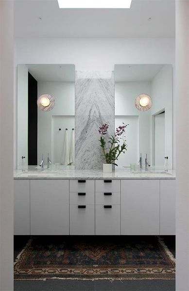 The primary bath features floating cabinets with book-matched Carrera marble countertop. Specialty lights through the mirrors display matching marble reveals.