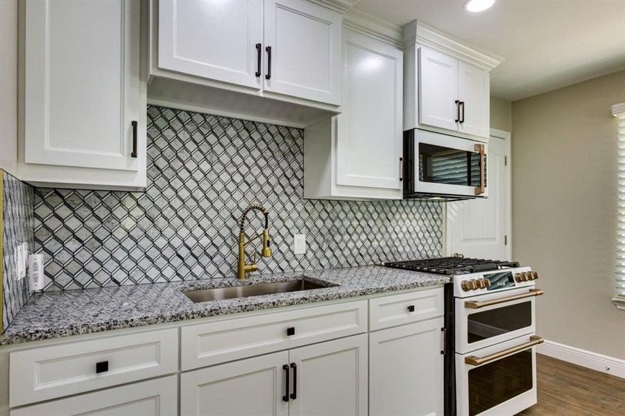Kitchen with range with two ovens, stainless steel microwave, light stone counters, white cabinetry, and recessed lighting