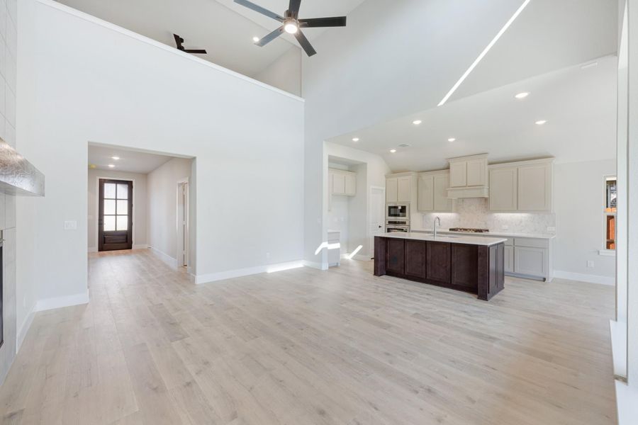 Open-concept living area with vaulted ceiling, ceiling fan, and kitchen featuring dark island and white cabinets with light wood floors