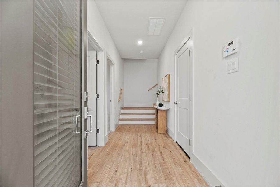 Welcome to a sleek, minimalist entryway with light wood floors and crisp white walls. The clean-lined corridor leads to a set of stairs, setting the tone for the modern design throughout the home.