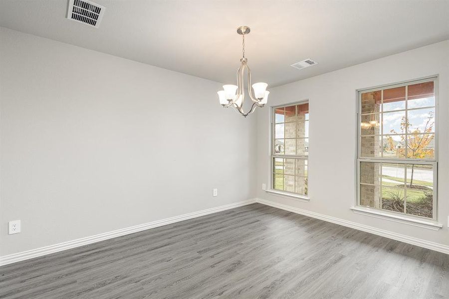 Empty room featuring an inviting chandelier, plenty of natural light, and dark wood-type flooring