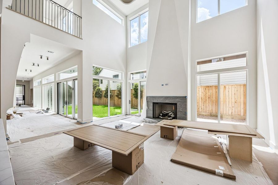 The living room is defined by soaring 24 ft. ceilings and expansive vertically, with clerestory windows positioned high above to draw in soft, natural light. A centrally positioned Gaslog fireplace anchors the west wall, full-height doors on either side of the fireplace and south wall, establish a seamless indoor-outdoor transition. Construction as of June 1, 2026.