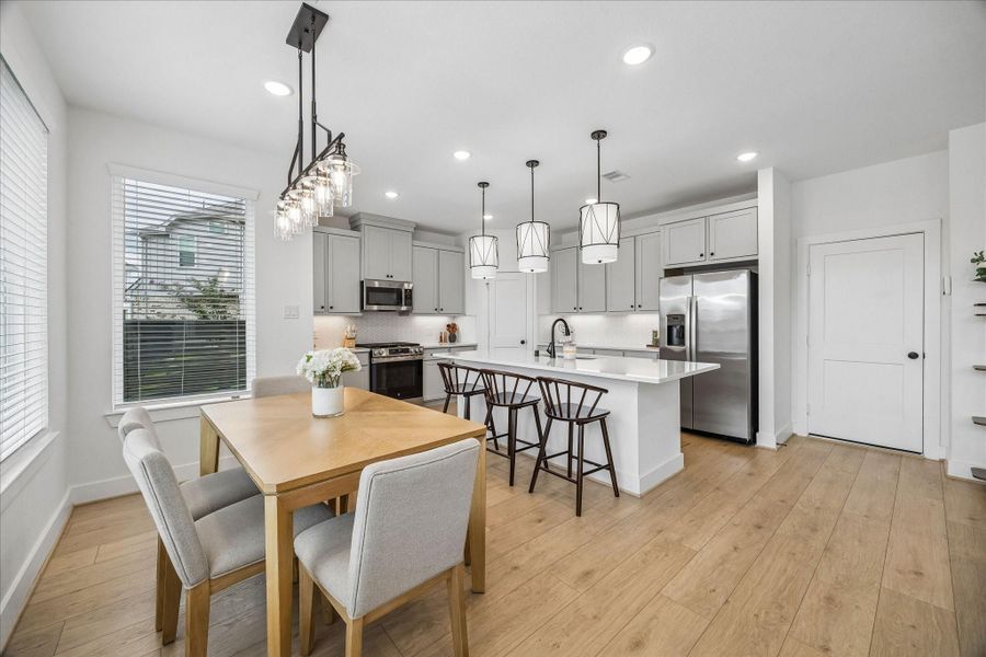 Light-filled open-concept kitchen and dining area featuring a spacious island with seating, abundant cabinetry, stainless steel appliances, and stylish pendant lighting. Convenient door provides easy access to the garage.