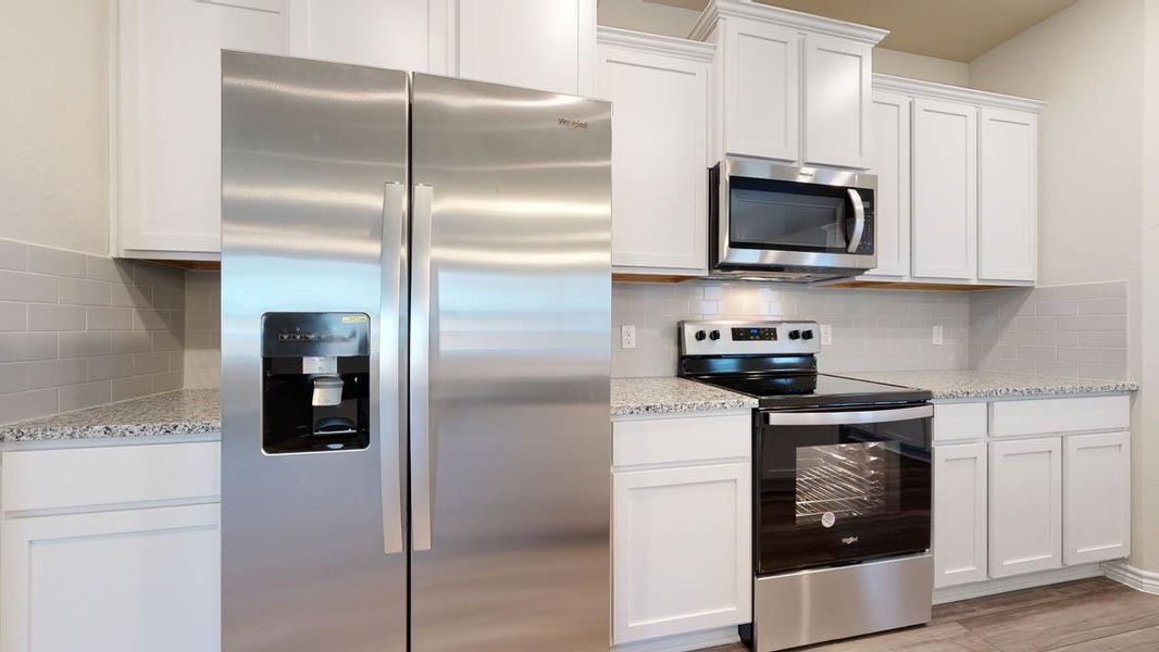 Kitchen featuring stainless steel appliances, white cabinetry, speckled countertops, and a subway tile backsplash