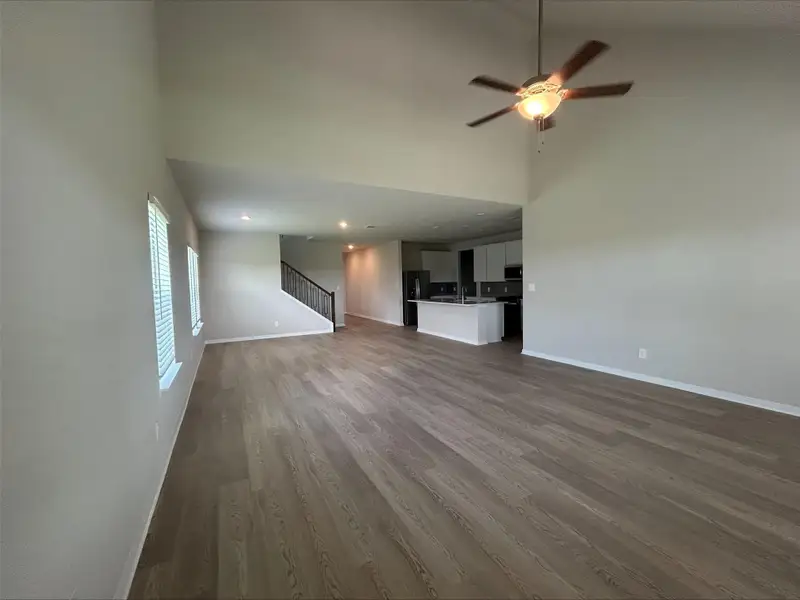 Unfurnished living room with a high ceiling, a ceiling fan, dark wood finished floors, stairs, and recessed lighting Unfurnished living room with a high ceiling, a ceiling fan, dark wood finished floors, stairs, and recessed lighting