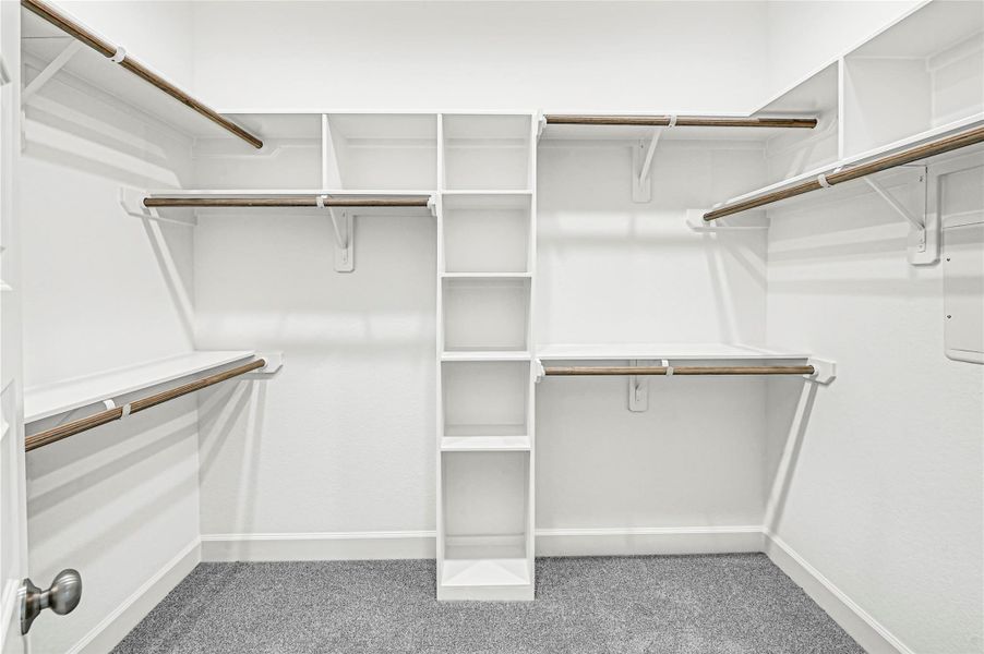 This photo shows a spacious walk-in closet with white shelving and multiple hanging rods, perfect for organized storage. The carpeted floor adds a cozy touch. This photo shows a spacious walk-in closet with white shelving and multiple hanging rods, perfect for organized storage. The carpeted floor adds a cozy touch.