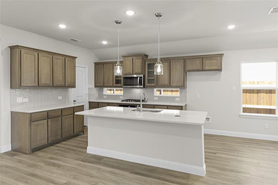 Kitchen featuring light hardwood / wood-style floors, hanging light fixtures, tasteful backsplash, a kitchen island with sink, and sink