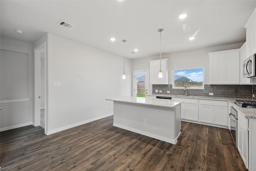 Kitchen with decorative backsplash, stainless steel appliances, a kitchen island, dark wood-style flooring, and recessed lighting