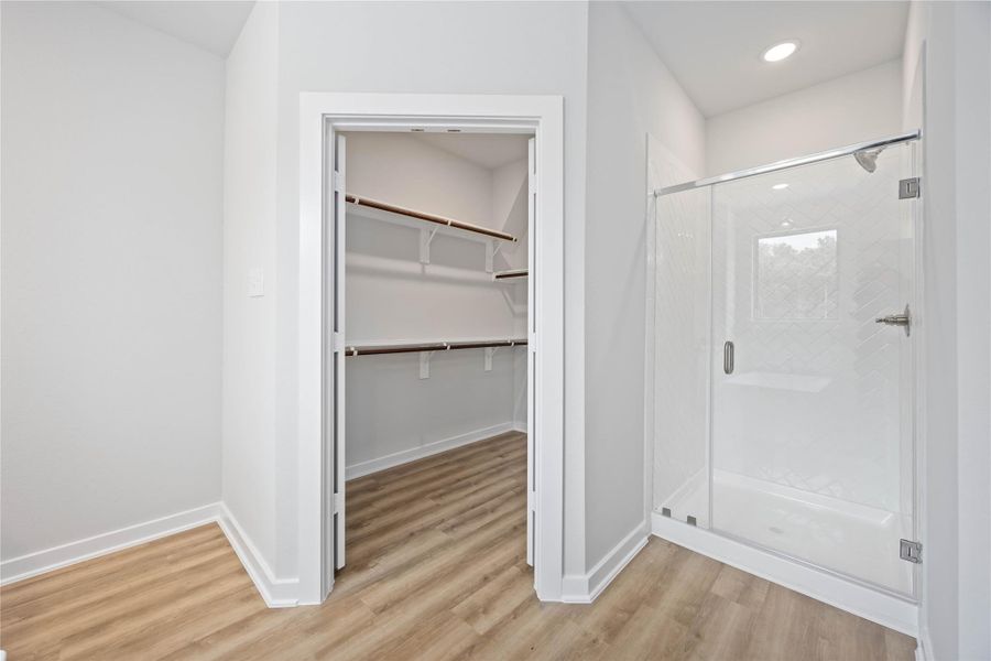 Neatly arranged primary closet with warm lighting and built-in storage options. Neatly arranged primary closet with warm lighting and built-in storage options.
