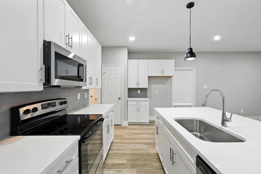 Kitchen with appliances with stainless steel finishes, tasteful backsplash, hanging light fixtures, light wood-type flooring, and white cabinetry Kitchen with appliances with stainless steel finishes, tasteful backsplash, hanging light fixtures, light wood-type flooring, and white cabinetry