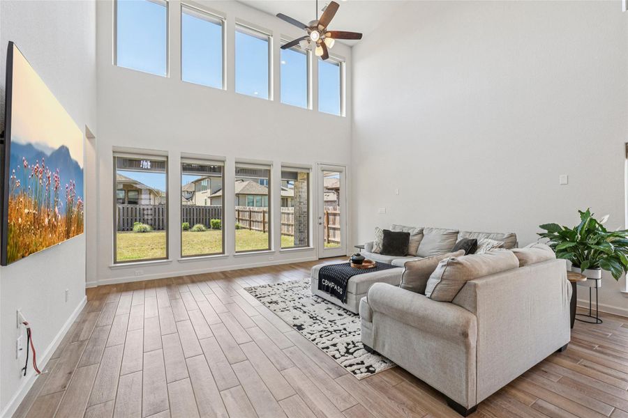 Living area featuring light wood-look flooring, high ceilings, and an array of windows providing abundant natural light and views of the backyard