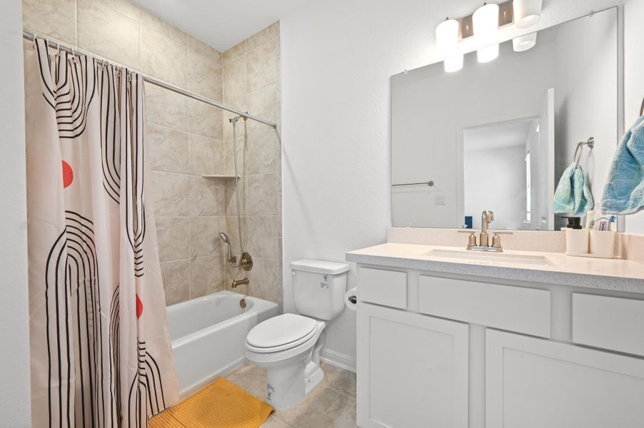 Tiled walls surround the shower and tub adjacent to a white vanity with stone countertops.